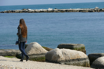 Naklejka na ściany i meble Giovane donna che passeggia in riva al mare in una bella giornata di primavera
