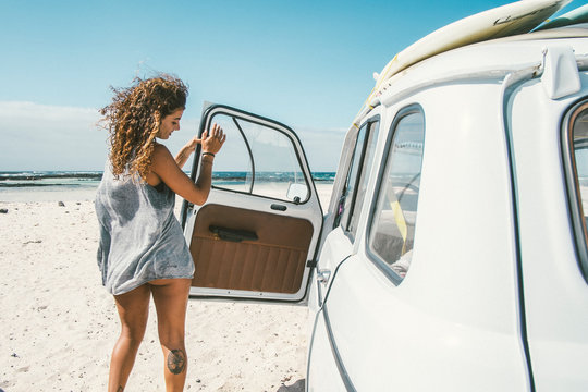 Beautiful female surfer standing next to her vintage car on the beach