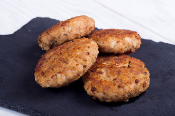 cutlets on a black flat plate, on a white wooden background