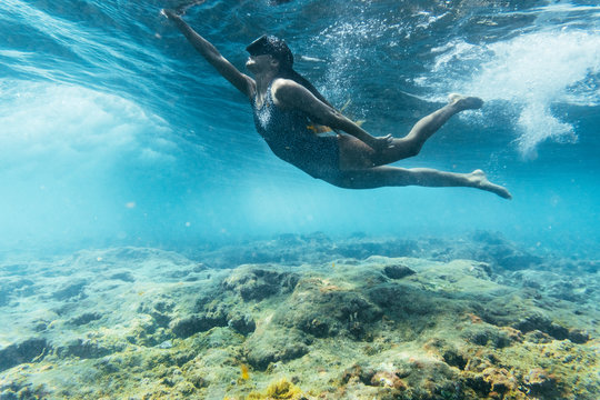 woman in a swimsuit and diving googles playing with the waves on the beach
