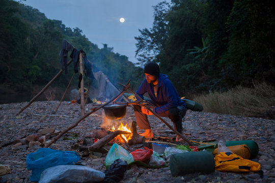 Man cooking over campfire while camping on the Nam Ou River in Phou Den Din National Protected Area, Phongsaly, Laos