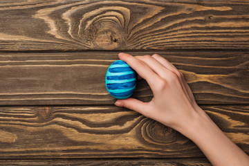 top view of woman holding easter egg with pattern on wooden surface