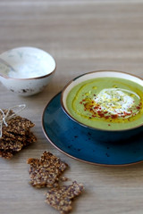 Creamy vegetable soup with kale, cabbage, celery and millet, decorated with olive oil, yoghurt sauce and chilli flakes. Served with seed crackers and lemony yoghurt sauce. Selective focus.