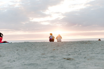 Two People Watching the Beautiful and Serene Sun Set Over the Ocean Horizon While Sitting in the Sand at the Tropical Beach