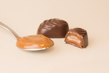 Artisan dark chocolate sweets isolated, opened with its filling on white background, with a full spoon of caramel filling