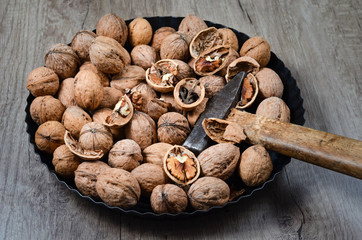 Rustic view  of whole and cracked   walnuts and a hammer  in a iron pan  , placed on a wooden table .