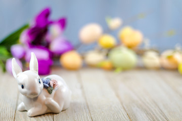 Spring Easter background on wooden board with white ceramic rabbit and colorful tulips and eggs room for text