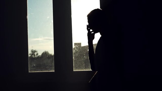 Close up shot of a silhouette young man stand near window walk sad nervous think sunset sunlight suicide in room slow motion