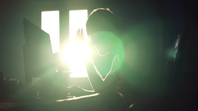 Silhouette young attractive tired man with glasses working use computer in the office communication sunlight computer designer internet male sunset technology networking online slow motion