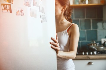 A young woman is looking into an open fridge while holding the door with her left hand. Diet concept.