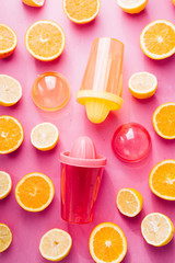 Orange and lemon juice maker, fresh summer juice, cut lemon and orange fruit with red and yellow juice container and squeezer,top view, on a pink board with strong backlight