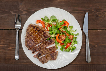 Grilled steak with vegetables on a plate with fork and knife on wooden background