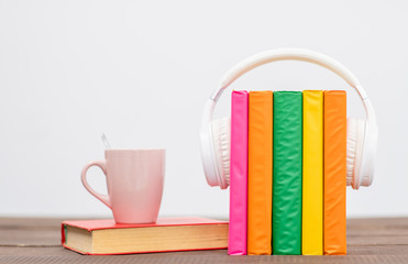 Fototapeta na wymiar Multicolored books with white headphones and coffe cup. Audiobooks concept. Empty space for text