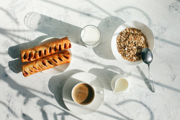 Breakfast from oatmeal with milk and cup of black coffee and rolls with jam and sunlight ray shadow on a gray table. Free space for text . Top view