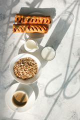 Breakfast from oatmeal with milk and cup of black coffee and rolls with jam and sunlight ray shadow on a gray table. Free space for text . Top view