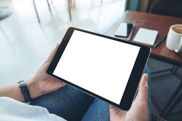 Mockup image of a woman sitting and holding black tablet pc with blank white desktop screen horizontally in cafe