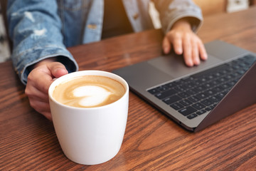 Closeup image of a woman using and touching on laptop touchpad on wooden table while drinking coffee