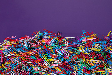 A variety of scattered colorful plastic paperclips with text space on a purple background