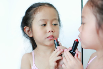 Adorable funny little girl applying lipstick over her mouth.