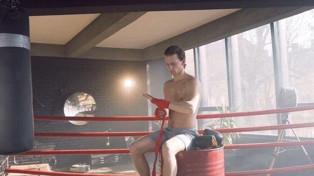 Attractive male boxer wrapping red bandages in the boxing club.