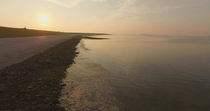 Aerial: The dykes and shoreline of the Oosterschelde, the Netherlands. Filmed during a hazy sunset.