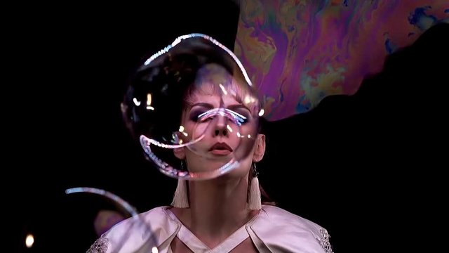 CU, Slow motion: Tricks with soap bubbles. A girl blowing a bubble towards the camera, through a soap screen. Glare colors of the rainbow, on the frame with LED backlight. Black background