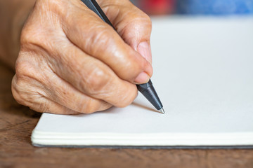 Senior woman's right Hand writing letter on ivory paper background, Notebook, A black pen, Close up & Macro shot, Selective focus, Stationery concept