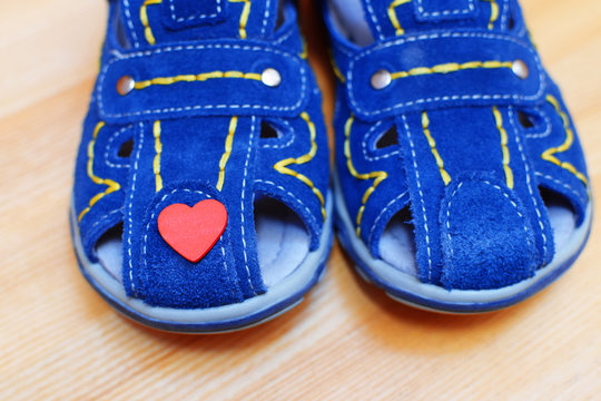 Blue Leather  Sandals Shoes For Baby Boy And Little Red Heart On Light Wooden Background Close Up View. Love And Family Concept.