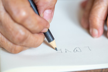 Senior woman's right Hand  writing " Love " on  ivory paper background, Close up & Macro shot, Selective focus, Stationery concept