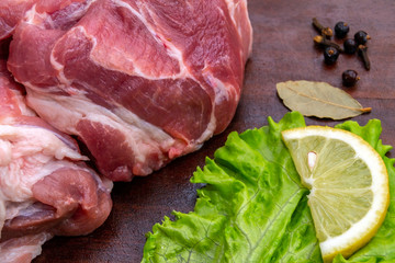  Pork meat, source of protein. Raw pork steak. On a cutting board, on a wooden table. With spices, herbs and lemon for cooking.  Side view.