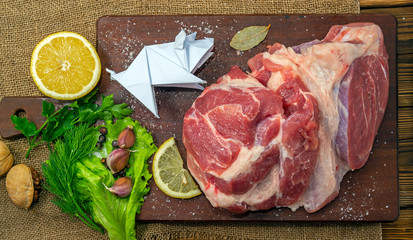 Pork meat, source of protein. Raw pork steak. Paper pig figure - origami. On a cutting board, on a wooden table. With spices, herbs and lemon for cooking. Copy space on top.