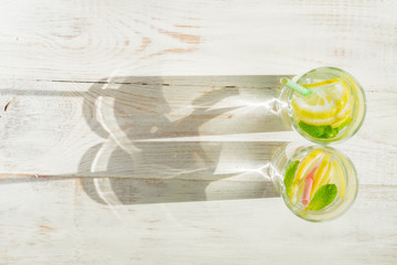 glass of homemade lemonade with lemons, mint and paper straws on wooden rustic background. Summer refreshing beverage. hard shadows