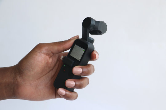 An Isolated Black African Hand Holding And Filming With A DJI Osmo Pocket Camera In Front Of A White Surface