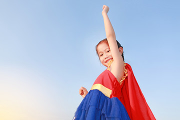 Superhero little girl in stance to fly on sky background at sunset light. Kid super hero concept.