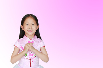 Happy little Asian child girl wearing pink traditional chinese dress with greeting gesture celebration for Chinese New Year isolated on pink-white background.