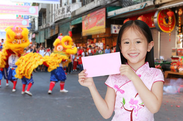 Happy little Asian child girl wearing pink traditional cheongsam dress smiling while receiving pink envelope packet on chinese festival background. Happy chinese new year concept.