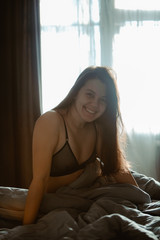 young pretty woman in black bra sitting on bed. morning time