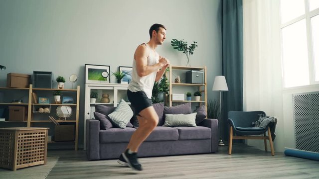 Handsome guy is exercising at home doing sports exercises for legs and body wearing comfortable sportswear and sneakers practising alone. Men, house and well-being concept.