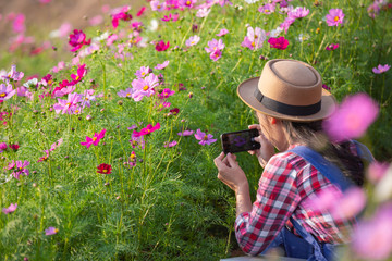 The girl is taking pictures of flowers with a mobile camera.