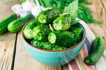 Marinated cucumbers with garlic and herbs in a ceramic plate on a wooden background