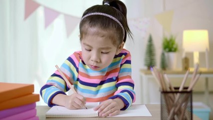 Kid's creativity, Child little asian girl writing in the book on the desk in the class room at home, Educational concept for school