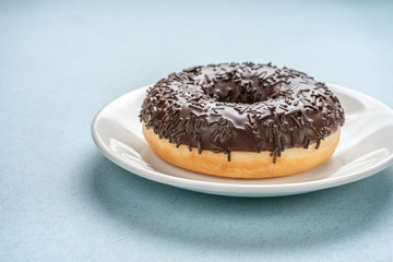 Chocolate donut on white plate on blue background.