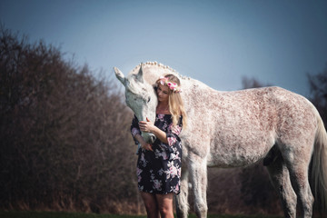 Portrait Frau und weißes Pferd Schimmel in Blumenkleid mit Blumenkranz im Haar im Wald in der...