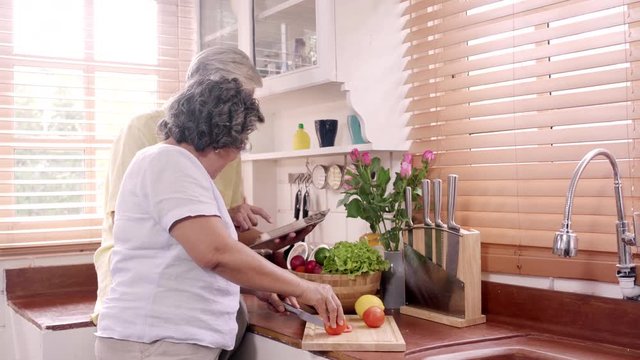 Asian elderly couple cut tomatoes prepare ingredient for making food in the kitchen, Couple use organic vegetable for healthy food at home. Lifestyle senior family making food at home concept.
