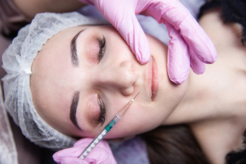 The doctor cosmetologist makes the Rejuvenating facial injections procedure for tightening and smoothing wrinkles on the face skin of a beautiful, young woman in a beauty salon.