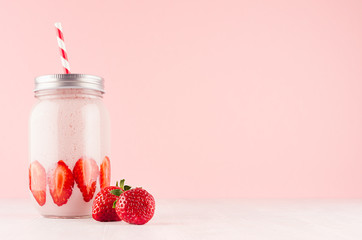 Summer fresh strawberry milkshake in jar with bright fruit, silver cap, red striped straw on elegance pink background, copy space.