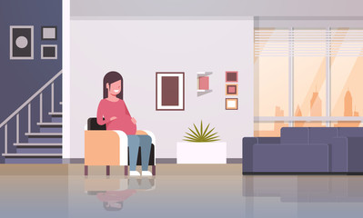 happy pregnant woman sitting in armchair girl holding her bump pregnancy and motherhood concept modern home living room interior flat full length horizontal
