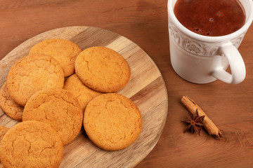 A closeup of ginger cookies with a mug of hot chocolate, a cinnamon stick, and an anise star on a dark rustic wooden background