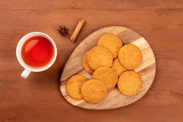 Gingersnaps, shot from the top with a cinnamon stick, an anise star, a cup of tea, and copy space on a dark rustic wooden background