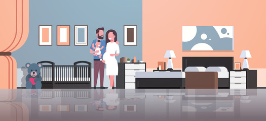 husband with pregnancy wife holding newborn baby son standing near crib happy family parenthood concept modern home bedroom interior flat full length